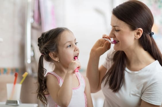 Mãe e filha escovando os dentes e olhando uma para a outra 