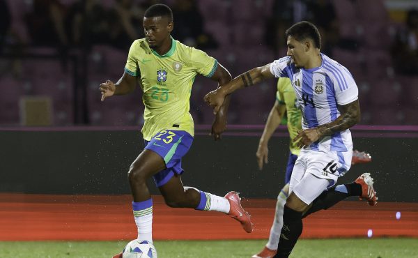 Alisson, do Brasil, em campo com a bola, enquanto Tobas Ramrez, da Argentina corre ao lado (foto: Foto: RAFAEL RIBEIRO/CBF)